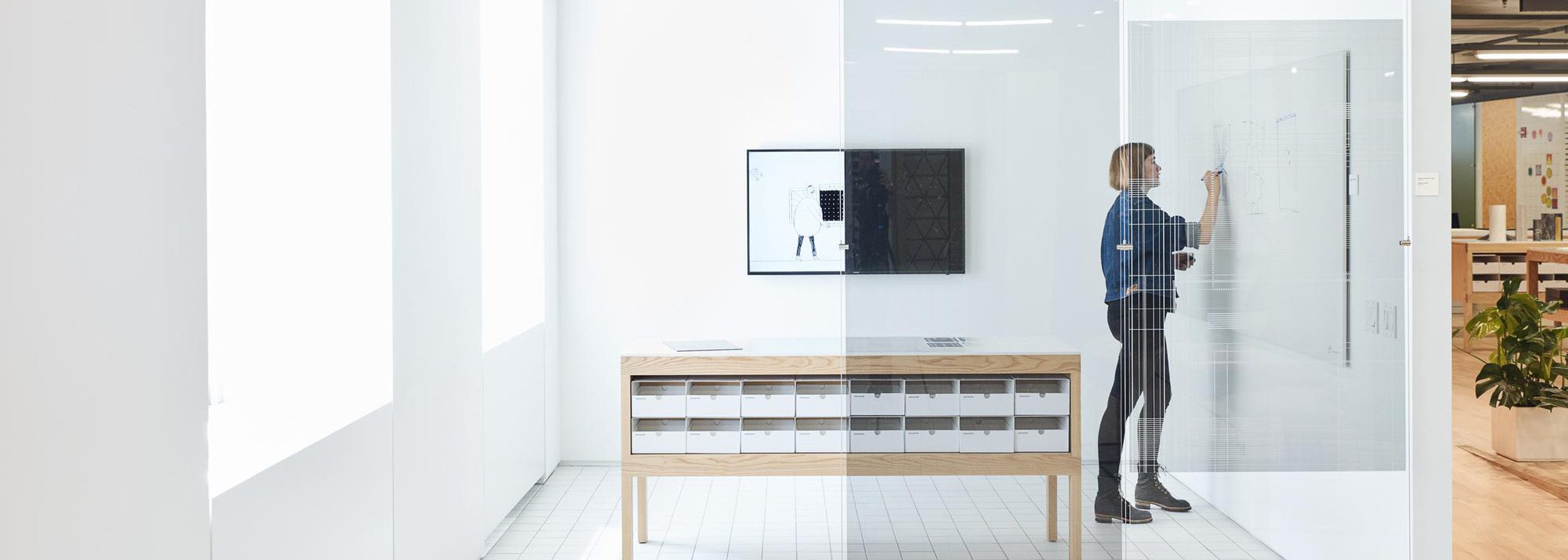 woman writing on board while tv screen is concealed by cloaking film on office windows
